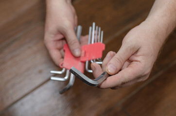 Hands hold a set of hex keys against the brown wooden floor. A g