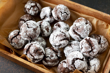 Homemade chocolate and coffee crinkle cookies in a wooden box on the kitchen table. Traditional American cookies for Christmas with cracks and powdered sugar on a dark background close-up