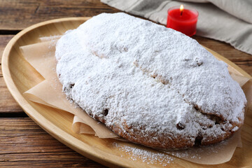 Wooden plate of delicious Stollen sprinkled with powdered sugar on table, closeup