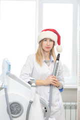 Portrait of a beautiful cosmetologist woman standing in a cosmetology office with a carbon peeling tool in her hands and a Santa Claus hat ready to celebrate Christmas and New Year and receive clients