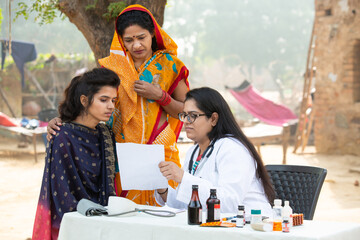 Young Indian adult girl with her mother getting proscription medicine by female doctor at village...