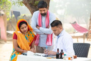 Indian Doctor prescribing medicine to the patient at village, woman wearing sari with her husband getting examine by medical person,Rural India healthcare concept.