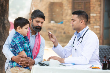 Indian Doctor examine little kid boy patient fever at village with digital thermometer, Father with...