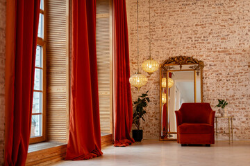 A modern French interior with corduroy burgundy curtains, an armchair, a vintage growth golden mirror and crystal chandeliers against a brick wall. Soft selective focus.