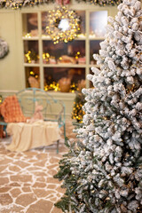 The snow-covered house is decorated for the new year. Vintage winter courtyard, decorated with New Year's decorations, Christmas trees, lanterns lights and a cozy bench. Soft selective focus.