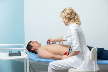 A cardiologist doctor applies sensors to the naked body of a man lying on a couch during an...