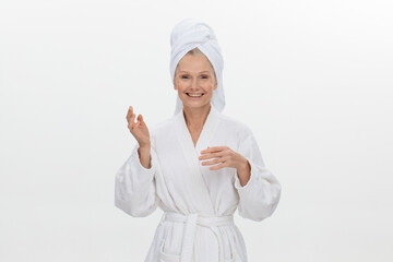 Close-up of a mature woman in a white bathrobe with a towel on her head applies