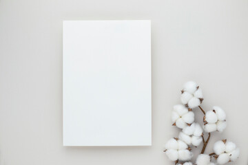 White invitation card mockup with a cotton flower on beige background, Minimal beige workplace...