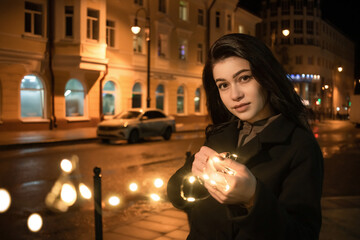 A lonely girl with glowing lights in her hands on the background of the night city.
