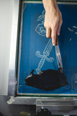 Top view of craftsman with ink spatula applying ink on screen printing machine 