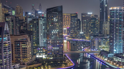 Fototapeta premium Dubai Marina with several boat and yachts parked in harbor and skyscrapers around canal aerial all night timelapse.