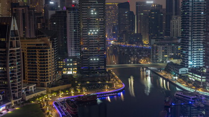 Fototapeta na wymiar Dubai Marina with several boats and yachts parked in harbor and skyscrapers around canal aerial night to day timelapse.