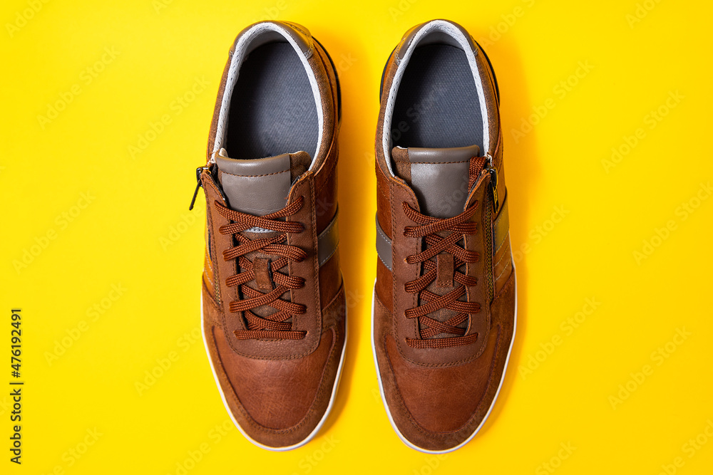 Wall mural pair of male's new sneakers made of brown leather on a yellow background. copy space. flat lay