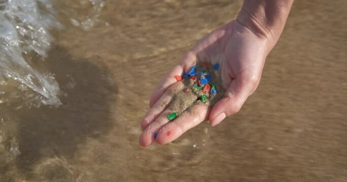 Parts of plastic in the sea. A woman takes sand with microplastic from the ocean water during summer vacation.
