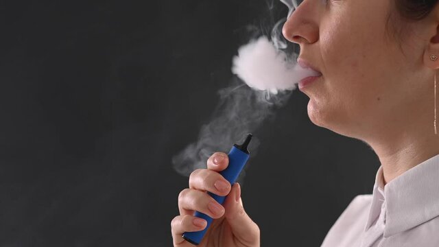 Caucasian woman smokes a disposable vape in the studio.