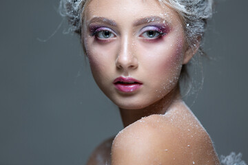 Winter Beauty Woman in clothes made of frozen flowers covered with frost, with snow on her face and shoulders. Christmas Girl Makeup. Make-up the snow Queen. Isolated on a gray background. Close-up.