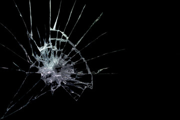 a crack on a broken glass mirror on a black background lines fragments bullet hole