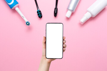 Hand with a smartphone and various toothbrushes, toothpaste and mouth freshener, on a pink...