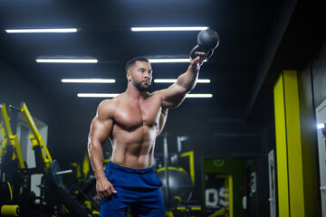 Naklejka na ściany i meble Portrait of a muscular sportsman performing kettlebell swings with one hand in a gym