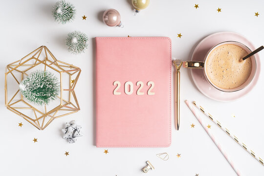 Top view Desktop Christmas pink notepad with 2021goals letters text. Flat lay of white table background with planner, cup of coffee, Christmas decoration, notebook and stationery.