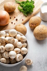 Ingredients for mushroom cream soup on grey table. Champignon, cream, potatoes, onions, parsley, salt and spices on wooden board. Top view.