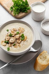 Bowl with mushroom cream soup, parsley, salt and croutons, toast on grey table. Champignon soup.