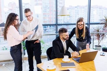 Successful handsome male mentor, director, businessman in a suit in an office with subordinates. Working day concept. Team meeting with the boss in the foreground