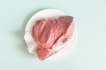 A piece of raw meat with onion slices on a white plate light blue background close-up