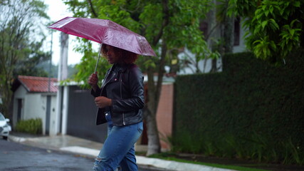 Young black woman holding pink umbrella outside during rainy day