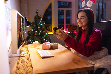Online celebration and Christmas holidays during quarantine life. Beautiful young girl talking with friends by means of video communication