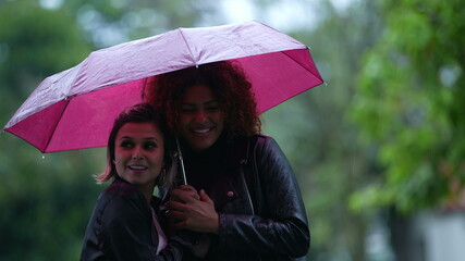Two young women sharing umbrella outside in the rain, friends covered by umbrella outdoors