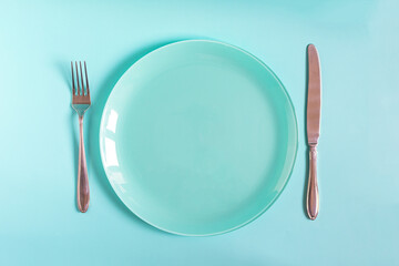 Table setting concept: a large blue plate and a fork with a knife on a blue background top view