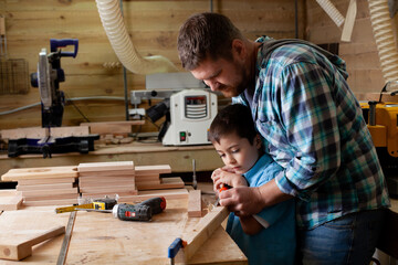 Father carpenter and son boy work in the workshop. Master dad teaches his son carpentry. Continuity...