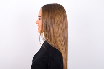 Obraz premium Profile of smiling Young caucasian girl wearing black turtleneck over white background with healthy skin, has contemplative expression, ready to have outdoor walk.