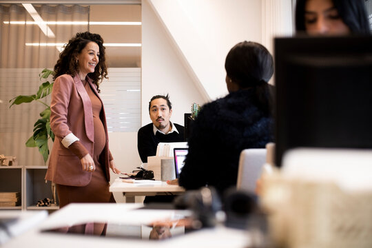 Smiling pregnant female manager discussing with colleagues in office