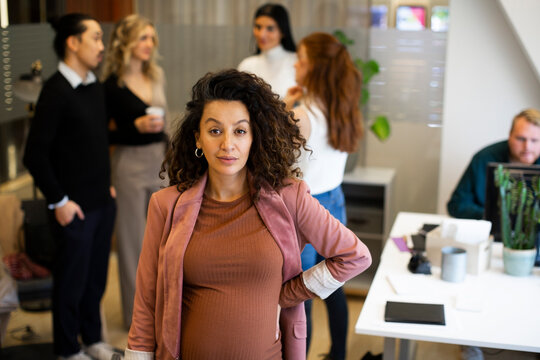 Portrait of pregnant businesswoman with colleagues in background at office