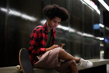 Portrait of happy african-american man with skateboard. Young fashion man using the phone.