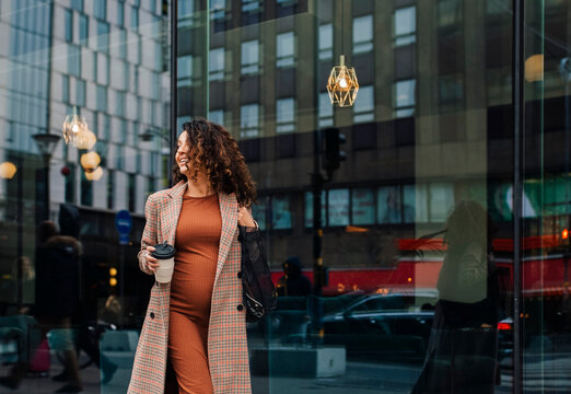 Pregnant businesswoman with disposable coffee cup looking away in city