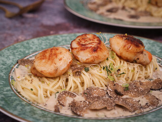 Close up of a plate of sear Scallops Spaghetti sliced black fresh Truffle  with mushroom truffle cream sauce. Spoon and fork in background. Truffles are seasonal from December to February 