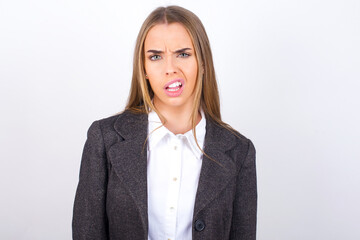 Portrait of dissatisfied Young business woman wearing jacket over white background smirks face,...