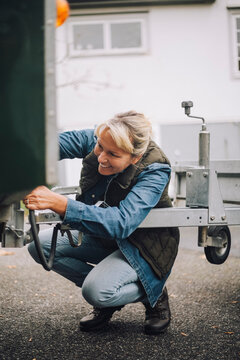 Smiling woman towing vehicle trailer on driveway