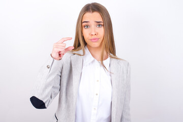 Displeased Young business woman wearing jacket over white background shapes little hand sign demonstrates something not very big. Body language concept.