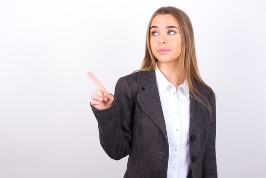 Young business woman wearing jacket over white background points at copy space and advertises something, advices best price.