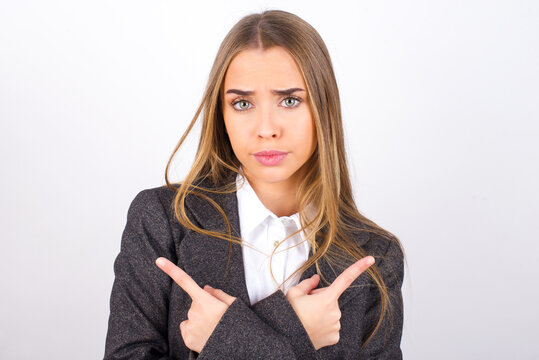 Serious Young business woman wearing jacket over white background crosses hands and points at different sides hesitates between two items. Hard decision concept