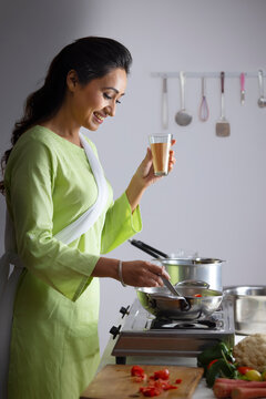 Young woman cooking vegetable in the kitchen with holding a glass of tea