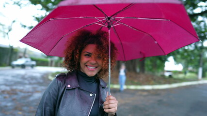 Brazilian woman holding umbrella walking outside in city during rain