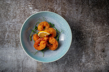 Serving a dish from the restaurant menu. Royal shrimp in batter with lemon and salad on a plate against a gray stone table, a tasty appetizer