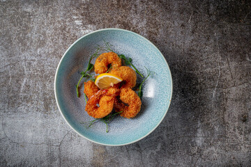 Serving a dish from the restaurant menu. Royal shrimp in batter with lemon and salad on a plate against a gray stone table, a tasty appetizer