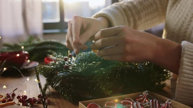 winter holidays, diy and hobby concept - close up of woman with ball decoration making fir christmas wreath at home