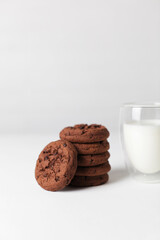 Brownie chocolate biscuits, homemade cakes. Milk in a glass on a light background.
Copy space, white background.